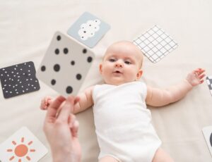 A baby lying on the floor looking up at a spotted card toy by Done by Deer