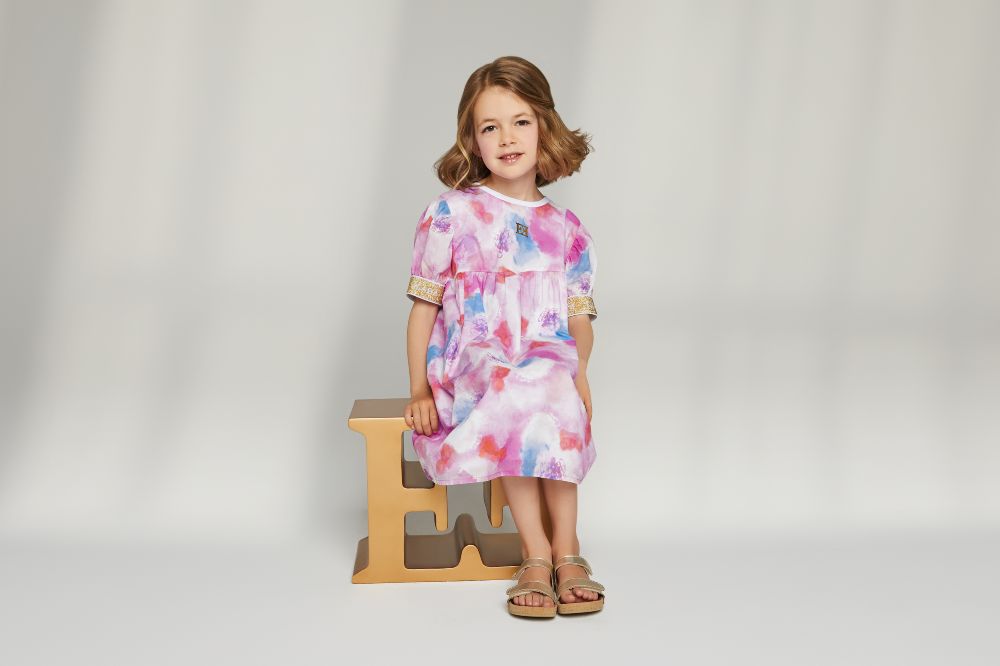 A young girl sat on gold E's wearing a floral dress by Escada Girls 