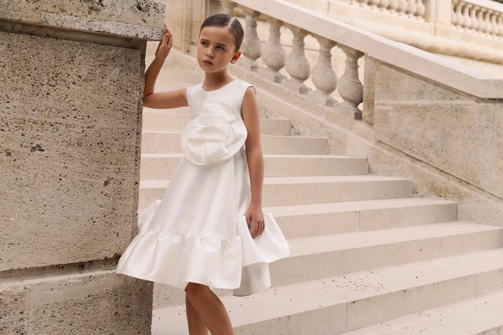 A girl stood outside steps of a building wearing a white special occasion dress by Gio Bespoke at Anthropologie