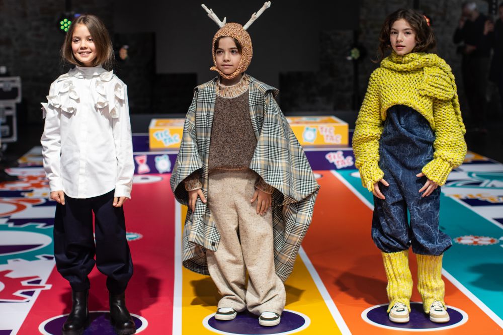 Three children stood on a catwalk at Pitti Bimbo wearing brightly coloured clothing 