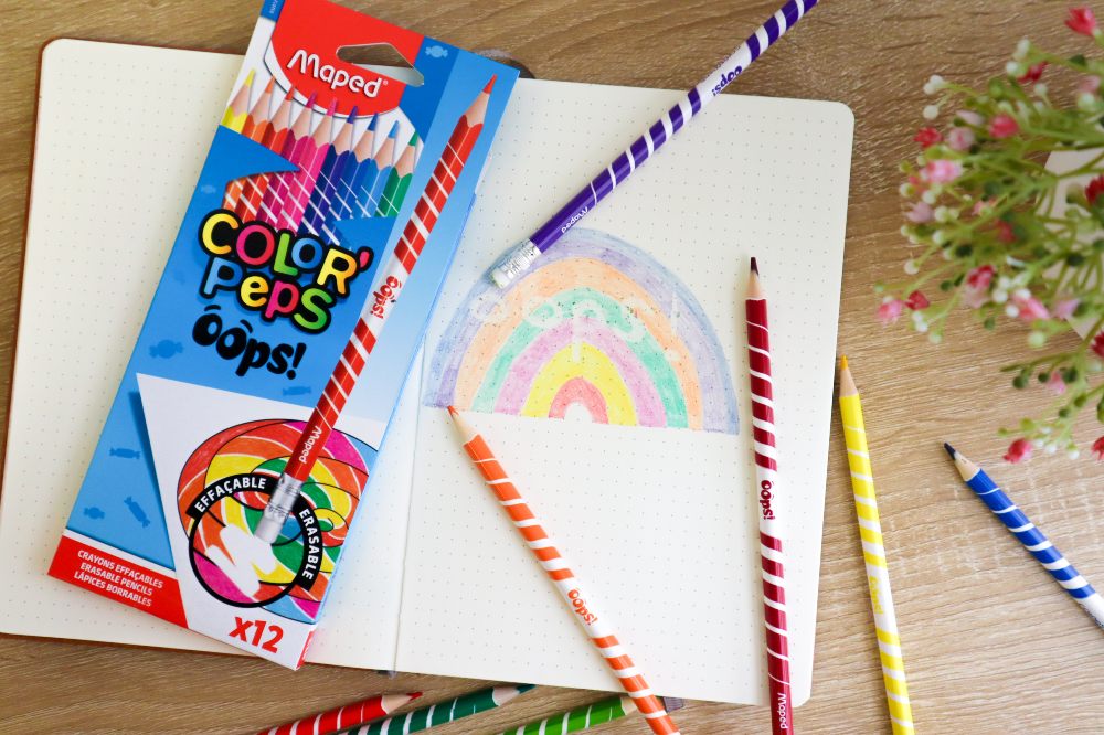 A notebook with a child's drawing beside a box of colouring pencils