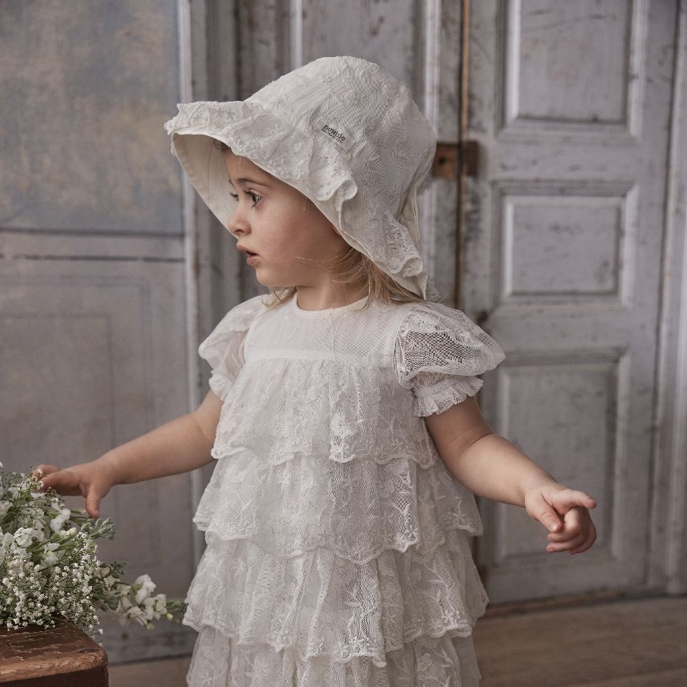 A young child in a white lace dress and hat