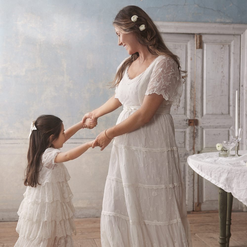 A woman in a wedding dress dancing with a young girl in a white lace dress
