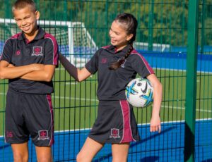 A boy and girl stood together on a sports playing field wearing school sports kits
