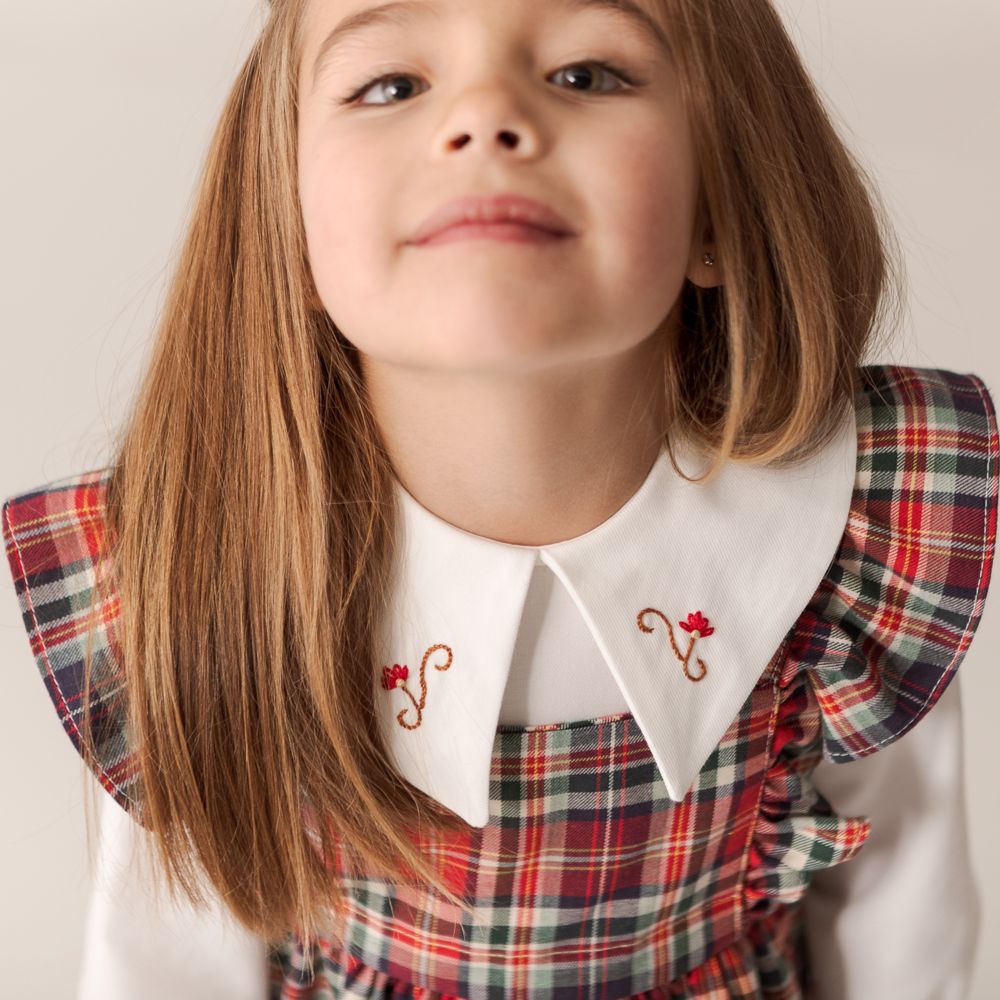 A young girl wearing a red tartan dress with a large white embroidered collar 