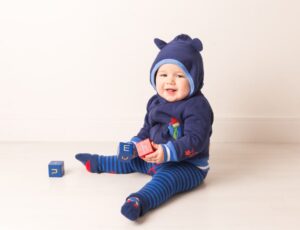 A young baby sat on the floor playing with wooden blocks wearing a Paddington Bear hoodie and leggings by Blade & Rose