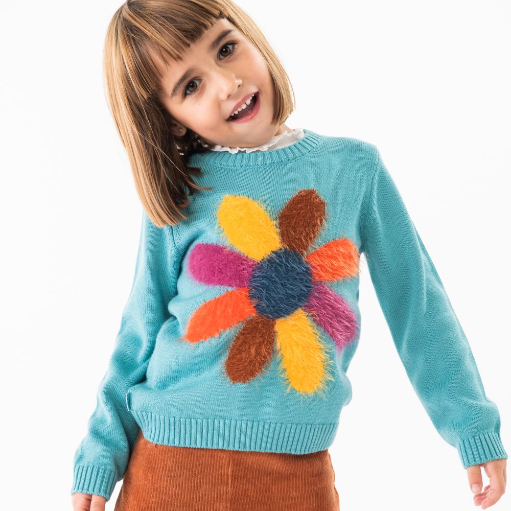 A young girl wearing a blue jumper with a large flower motif 