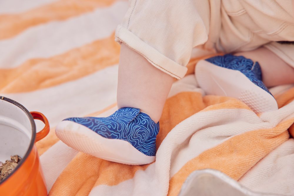 A close of a baby's foot in a blue shoe against an orange and white striped rug