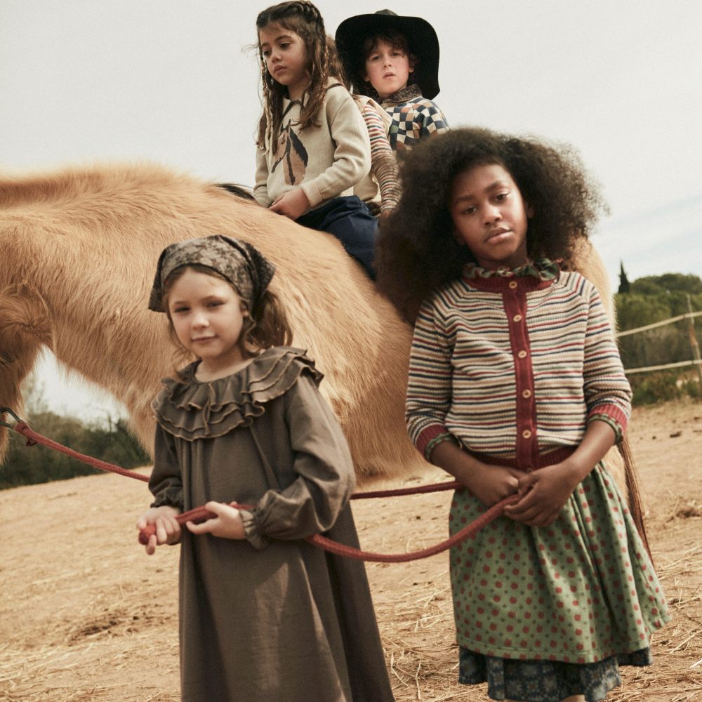 Two children sat on a horse with two young girls stood beside it holding the horse's rein 