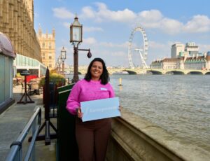 A woman stood beside the Thames holding up a board saying F:Entrepreneur as part of a celebration of female entrepreneurs