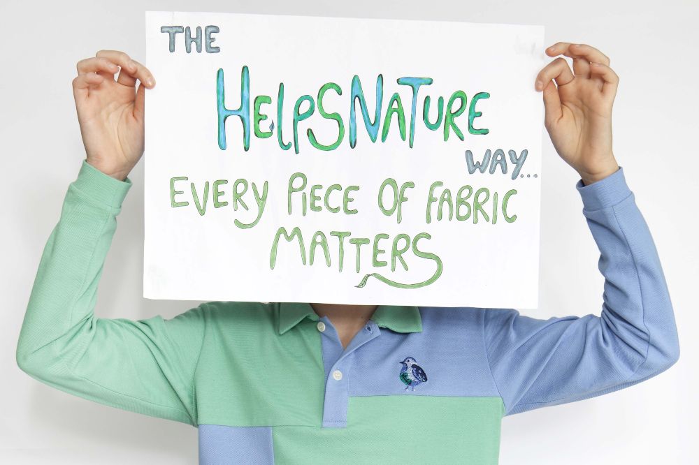 A child in a blue and green top holding a white sign in front of their face saying The Helps Nature Way Every Piece Of Fabric Matters