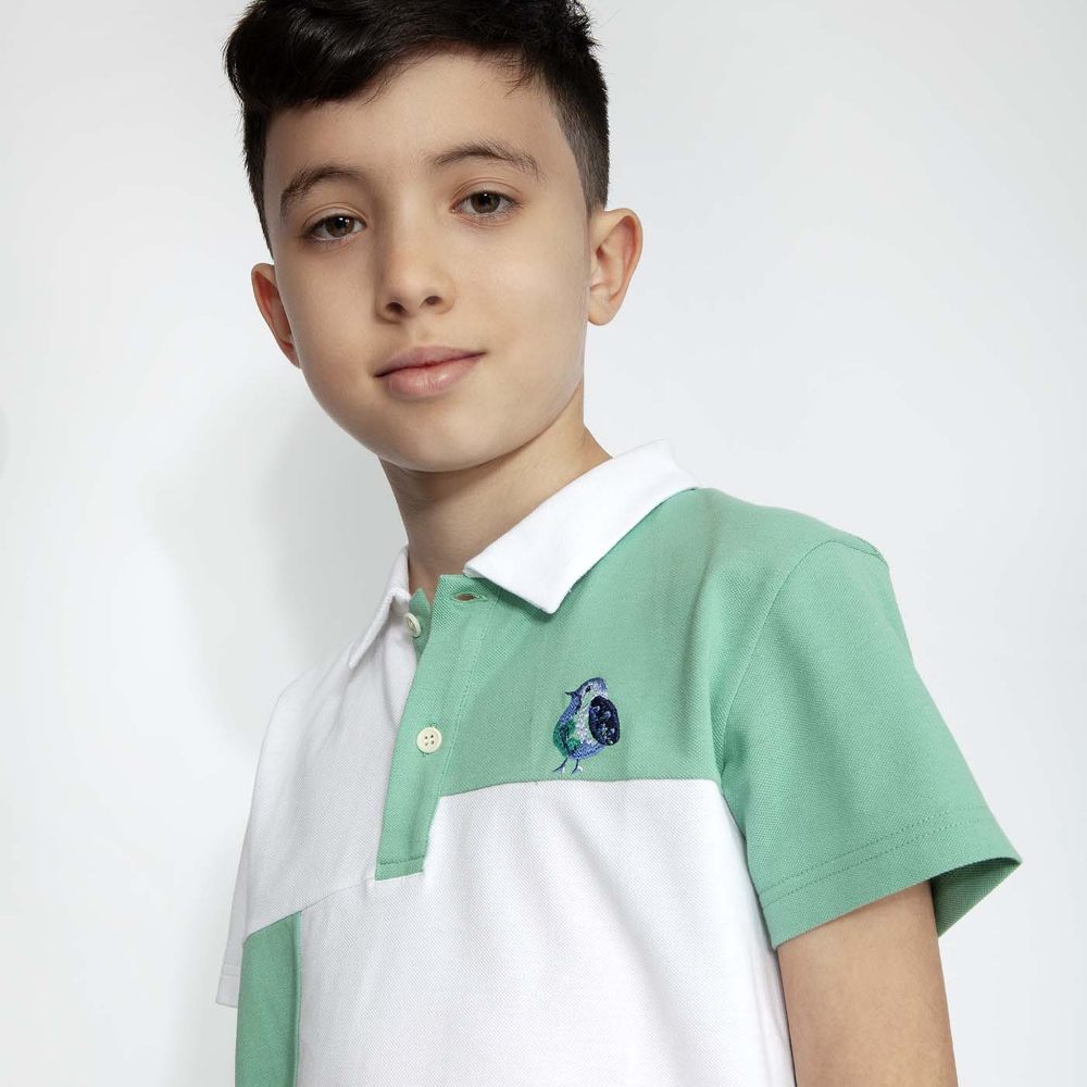 A boy wearing a green and white polo shirt with a blue bird logo on the front 