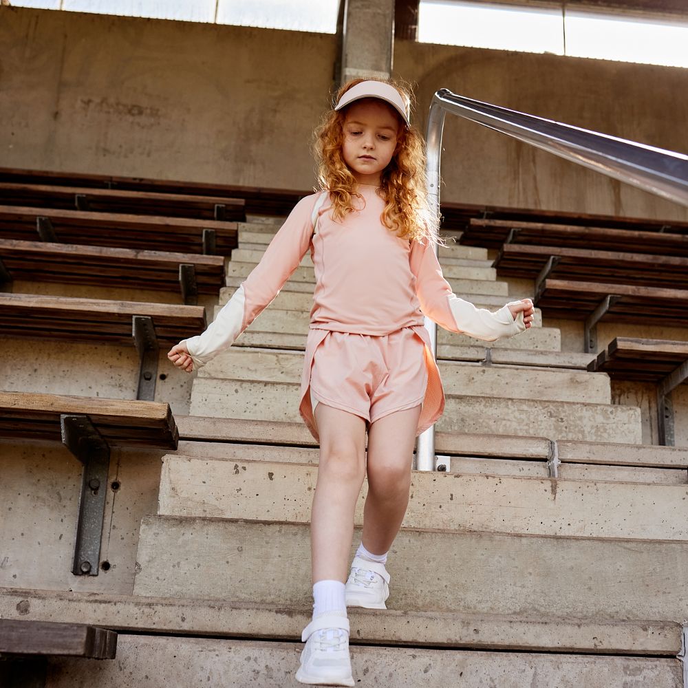 A young girl wearing a cap, T-shirt and shorts walking down the steps of a stadium 