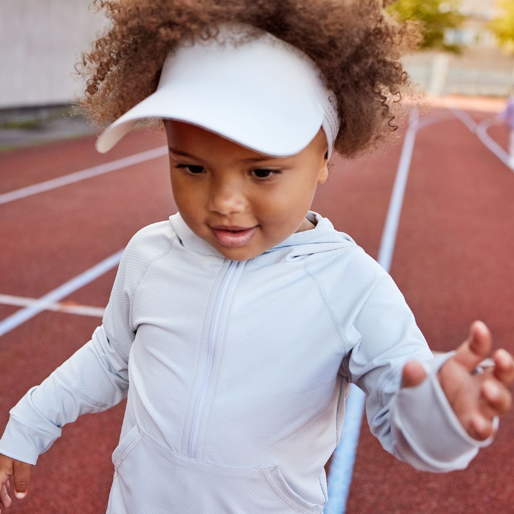 A young child on a running track wearing a sun visor and sports top 