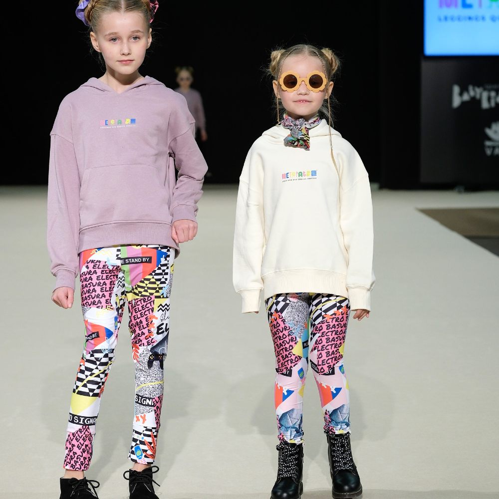 Two children stood on a fashion catwalk at Babykid Spain + FIMI wearing bright leggings and sweatshirts 