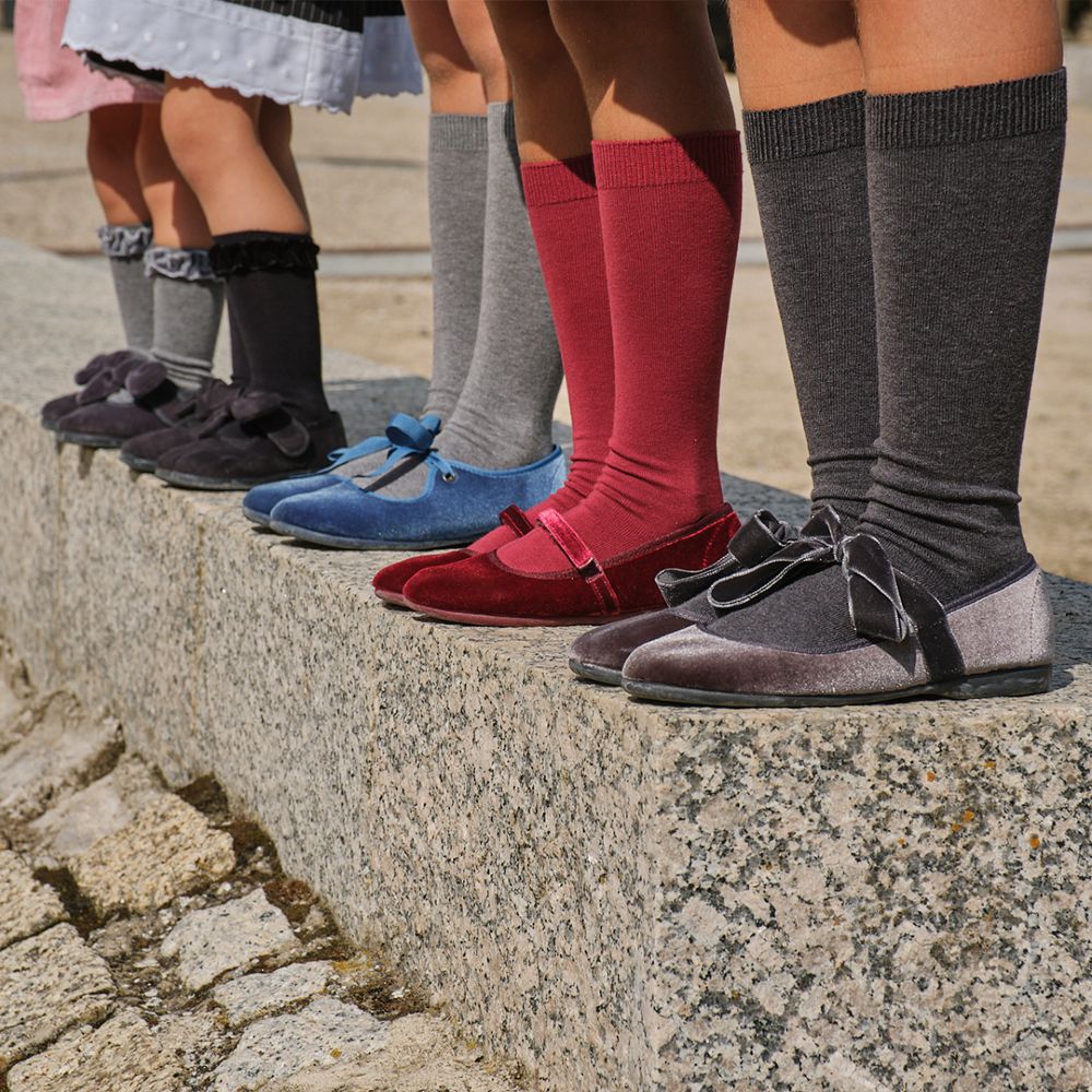 A picture showing children's legs wearing knee socks and different coloured velvet shoes 