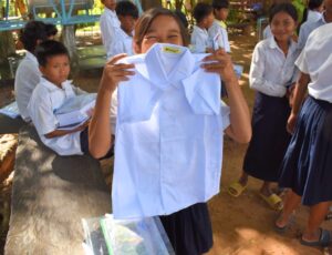 A Cambodian child stood outside holding up a white school shirt