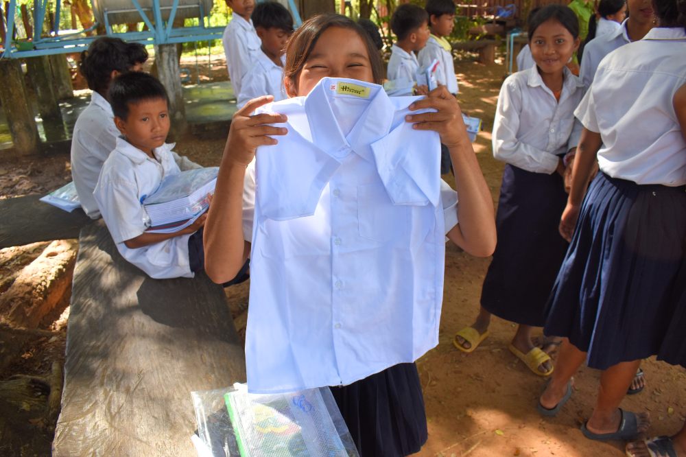 A Cambodian child stood outside holding up a white school shirt