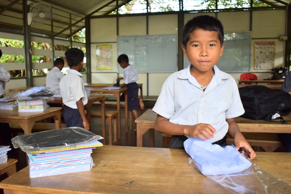 A young boy in a classroom in Cambodia stood in front of a school desk 