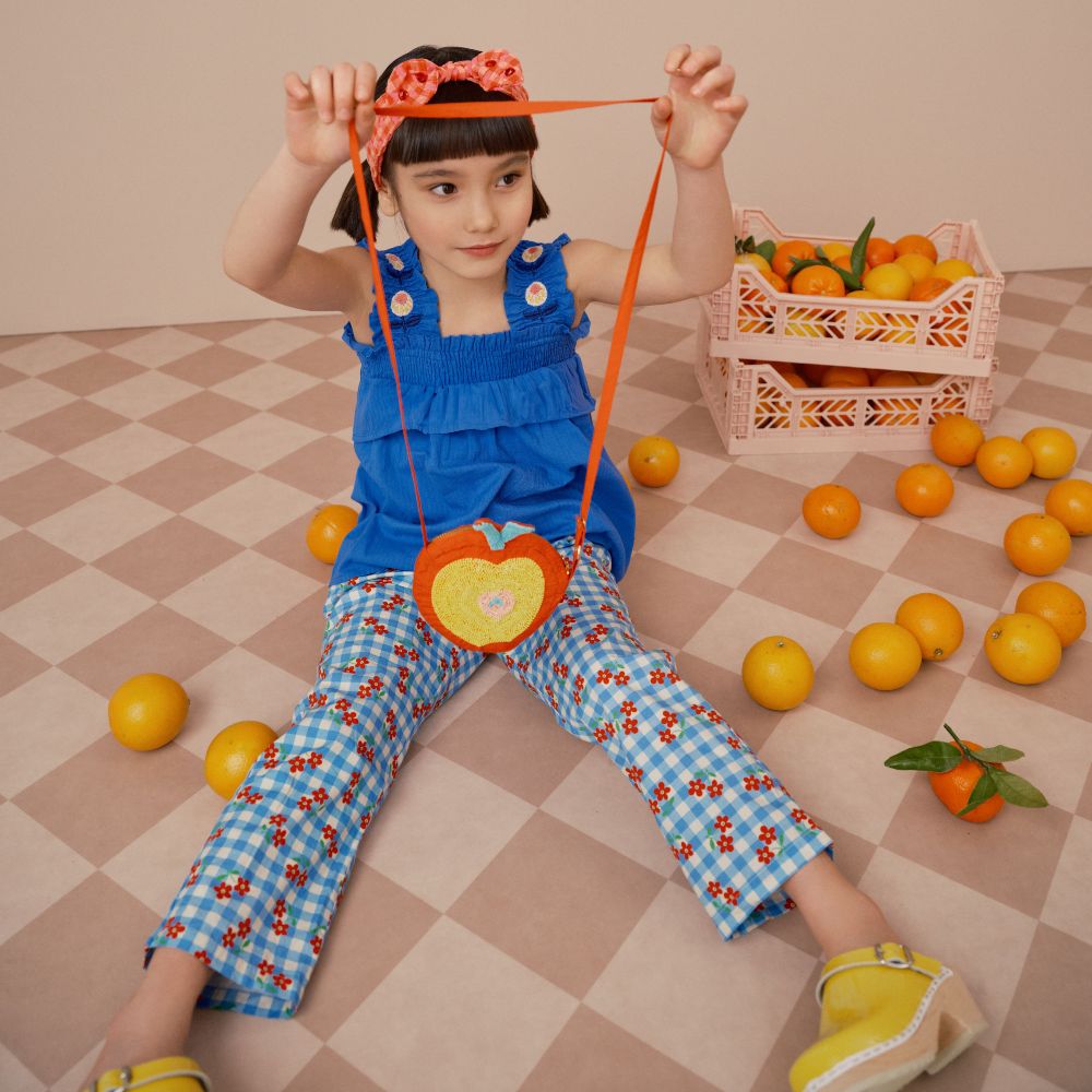 A young girl sat on the floor next to boxes of oranges holding up an apple-shaped bag 