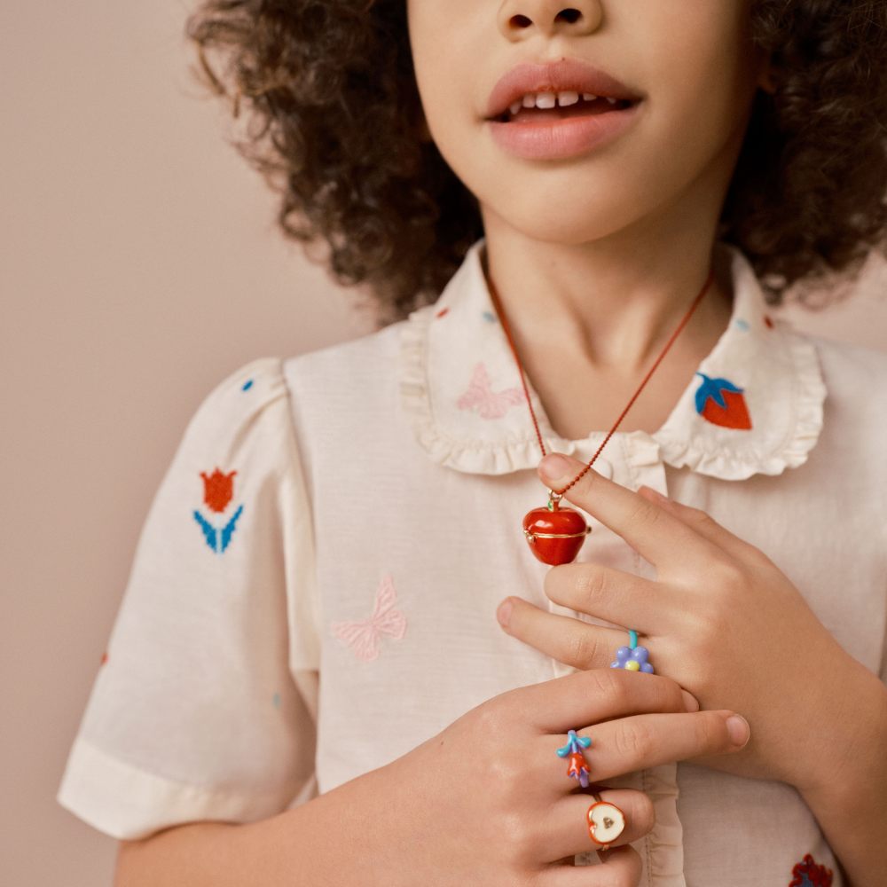 A girl wearing a blouse embroidered with red tulips and a red apple pendant necklace 