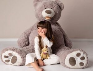 A child sat on the floor beside a large teddy wearing a white top and trousers by Adaptive Clothing UK