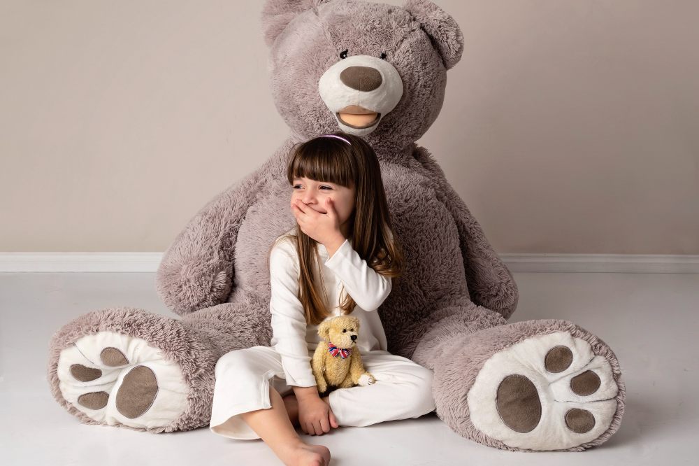 A child sat on the floor beside a large teddy wearing a white top and trousers by Adaptive Clothing UK