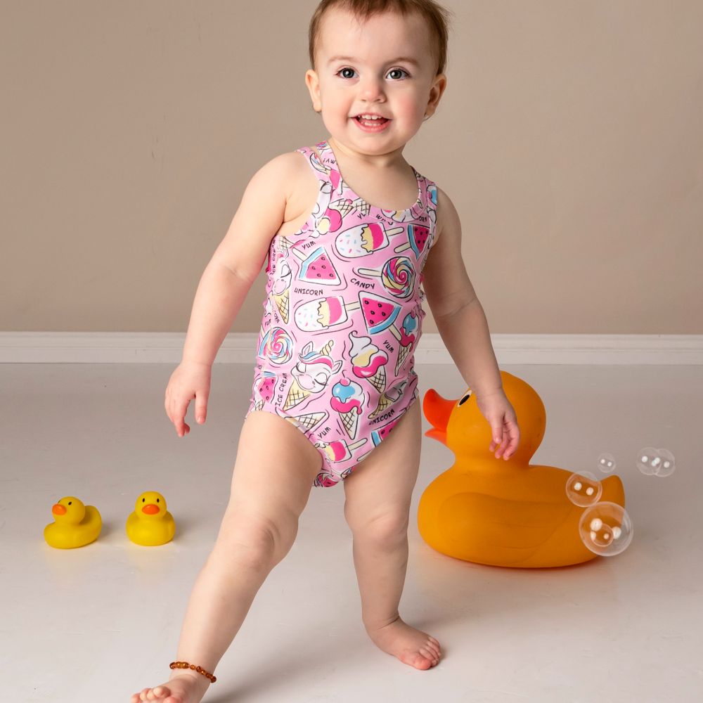 A baby stood in an adaptive pink swimsuit surrounded by yellow rubber ducks 