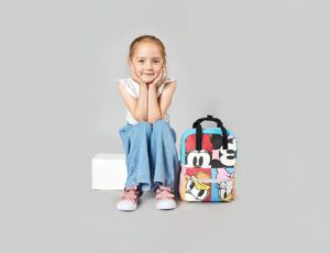 A young girl sat on a white box beside a Disney rucksack