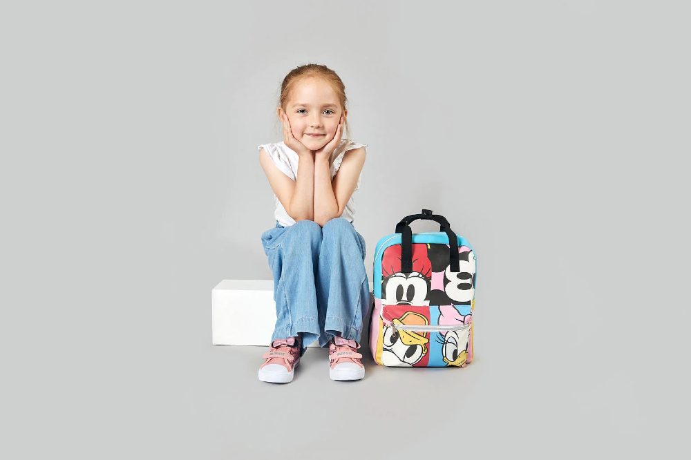 A young girl sat on a white box beside a Disney rucksack