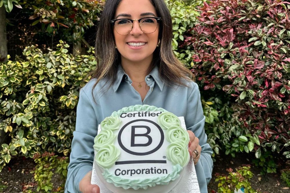 The founder of The Baby Gifting Company stood outside holding up a cake with Certified B Corporation written on it