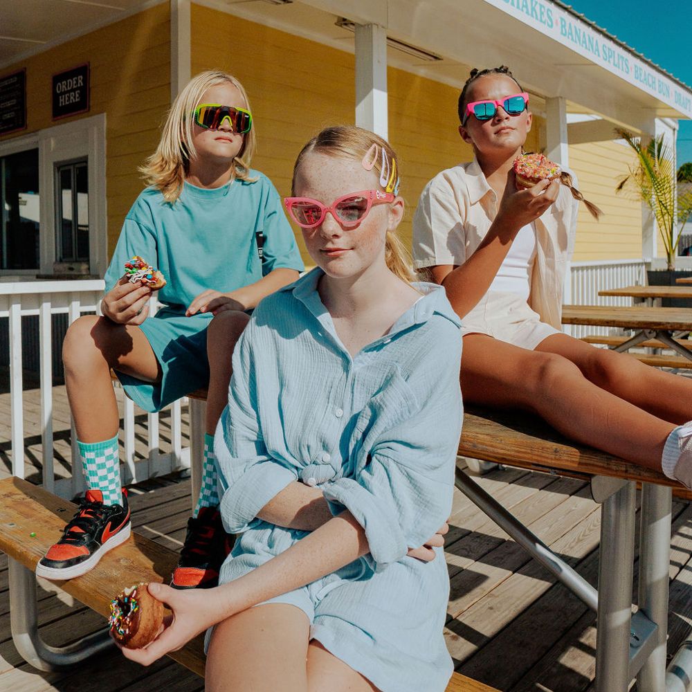 Three children in sunglasses sat outside at a picnic table 