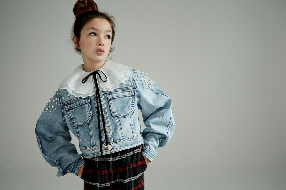 A girl looking upwards wearing a denim jacket with a white collar and tartan trousers 