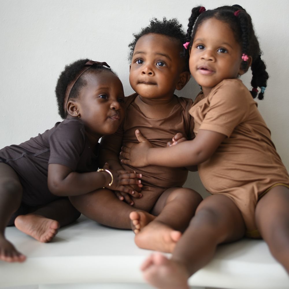 Three young children in babygros hugging each other 