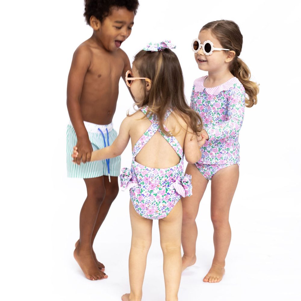 Three children in swimwear stood in a ring holding hands