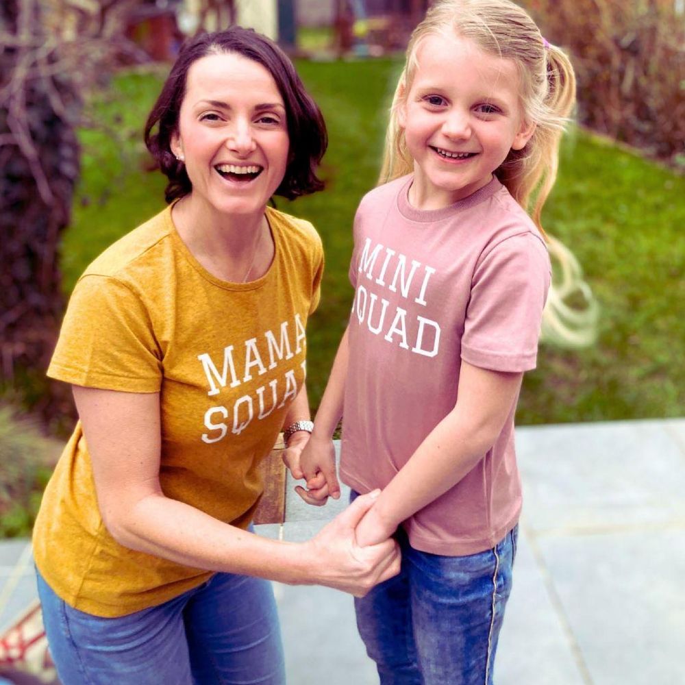 A woman and girl outside holding hands and smiling at the camera