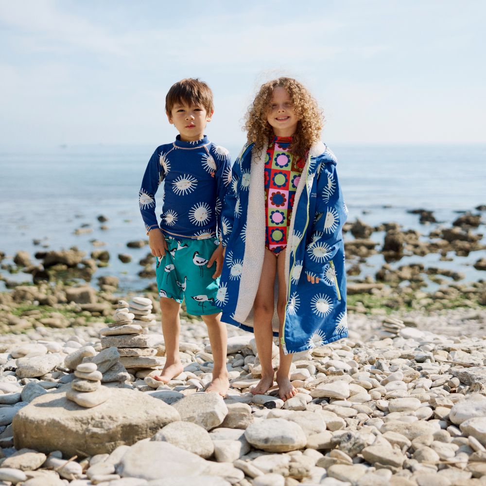 Two children stood on a beach wearing swimwear 