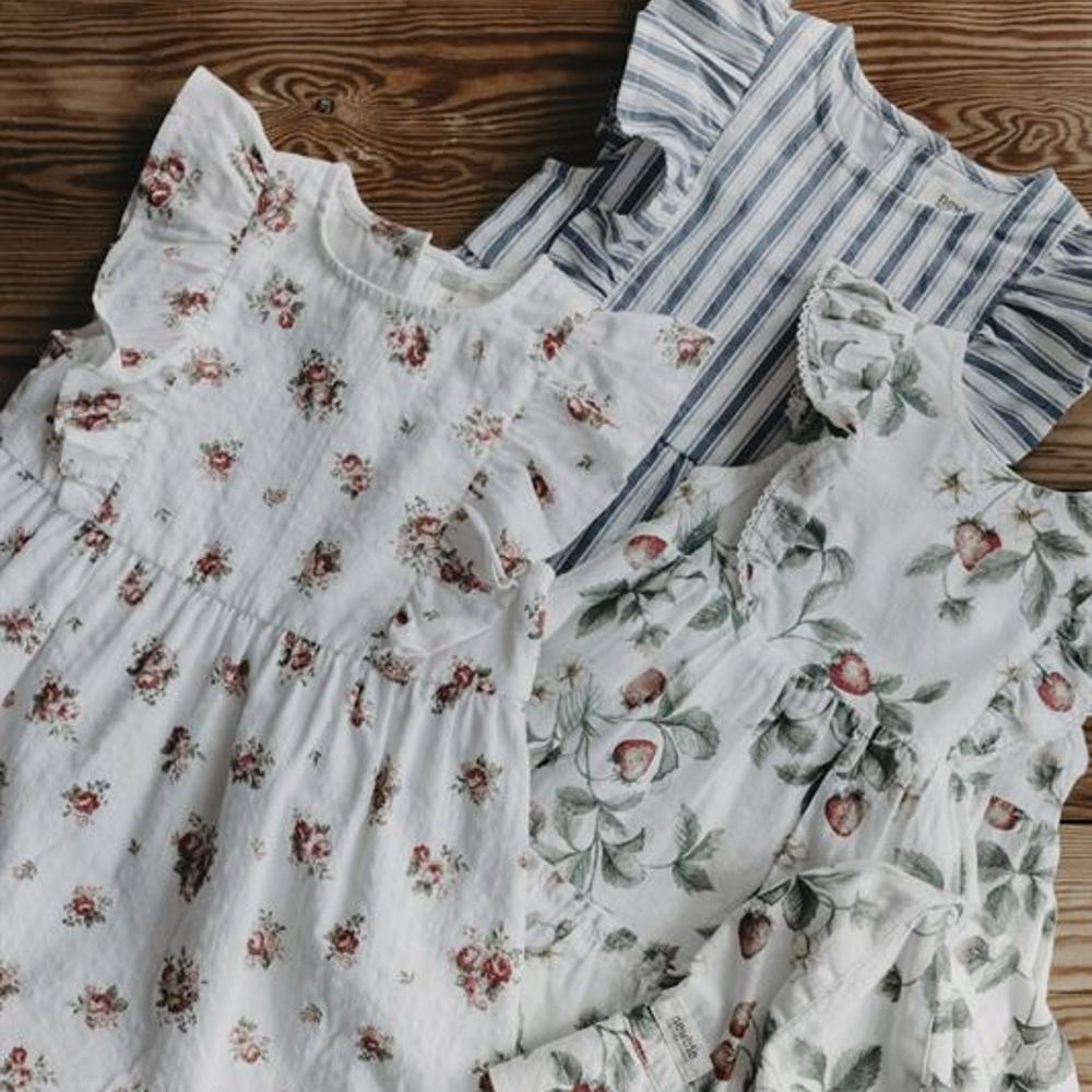 Three children's dresses laid on a wooden table 