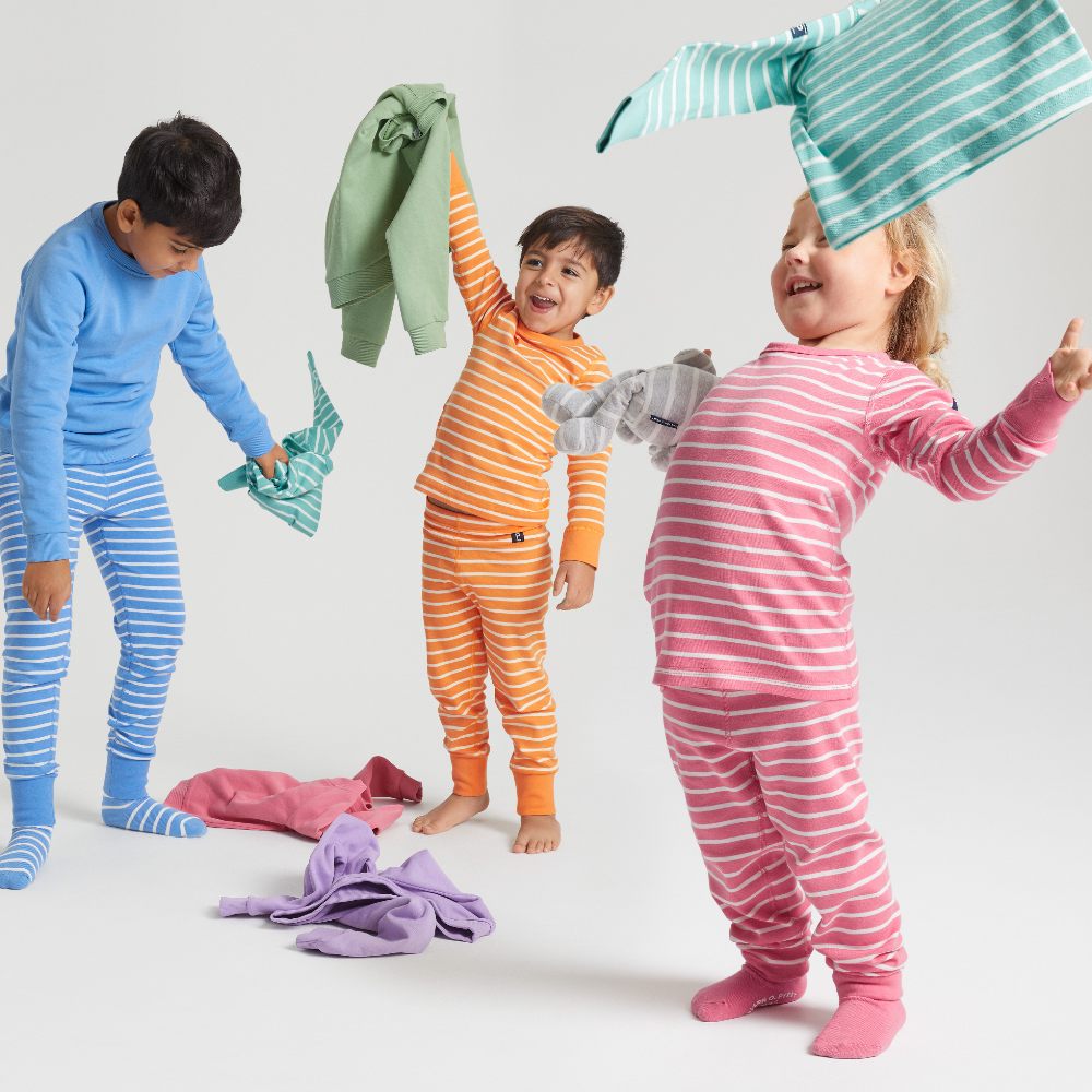 Children wearing different coloured striped tops and trousers throwing clothes in the air 