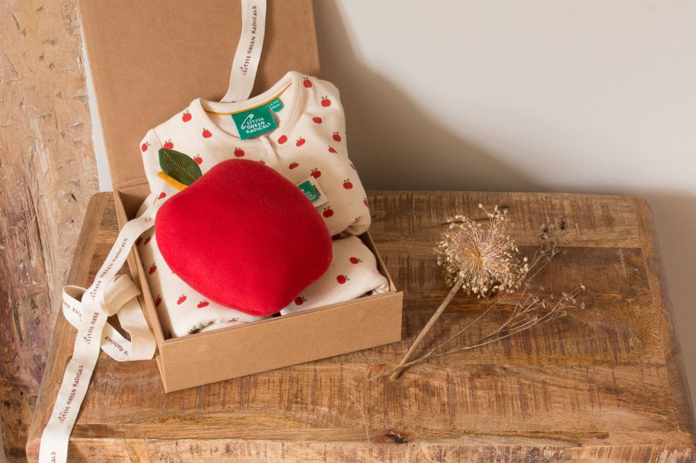 A box on a wooden table containing a child's top and a red apple soft toy 