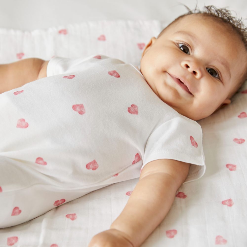 A baby lying down wearing a pink heat babygro by Rosa & Blue 