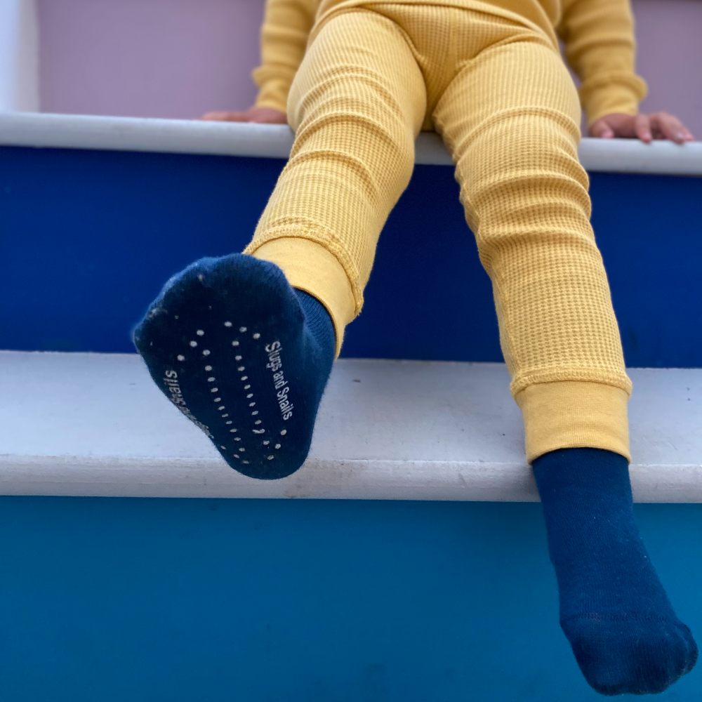 A child sat on blue steps wearing yellow footless tights and blue socks by Slugs & Snails