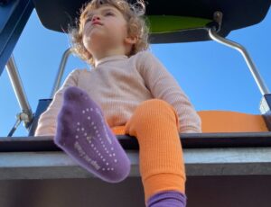 A child sat on a climbing frame wearing purple socks and orange footless tights by Slugs & Snails