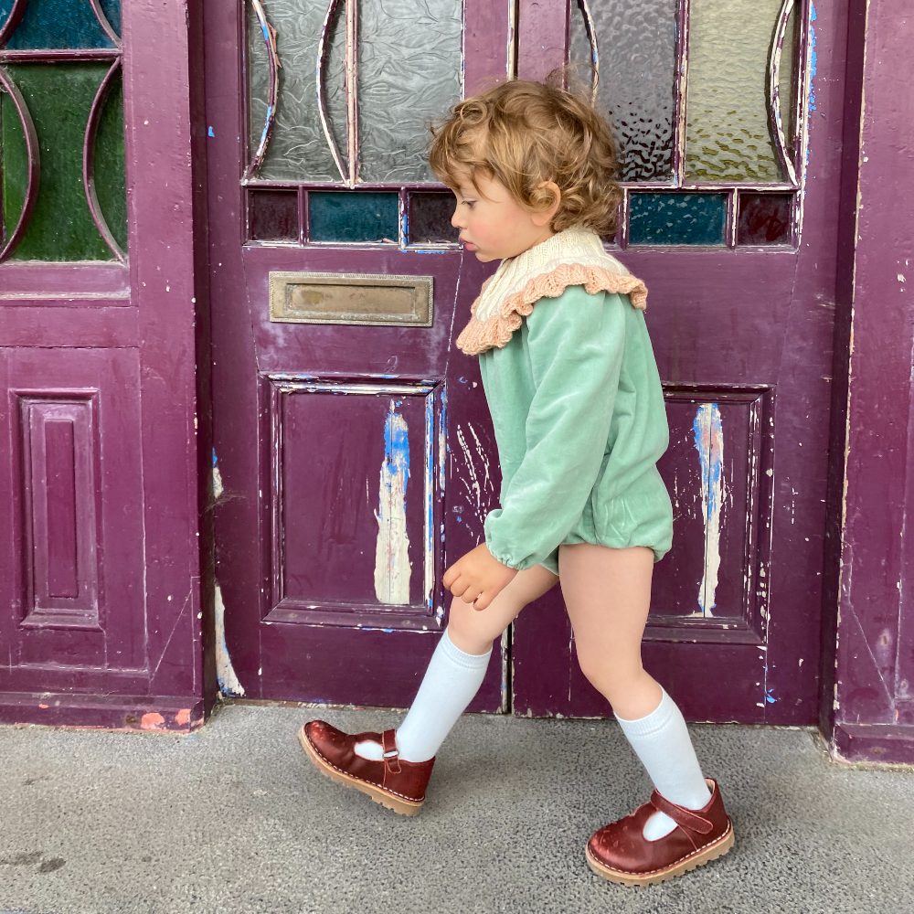 A child in knee socks walking past a purple door 