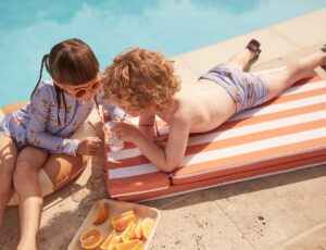 Two children beside a pool eating pieces of orange