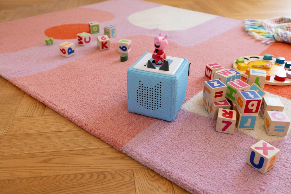 A blue Learn with Peppa Toniebox on the floor surrounded by toys 