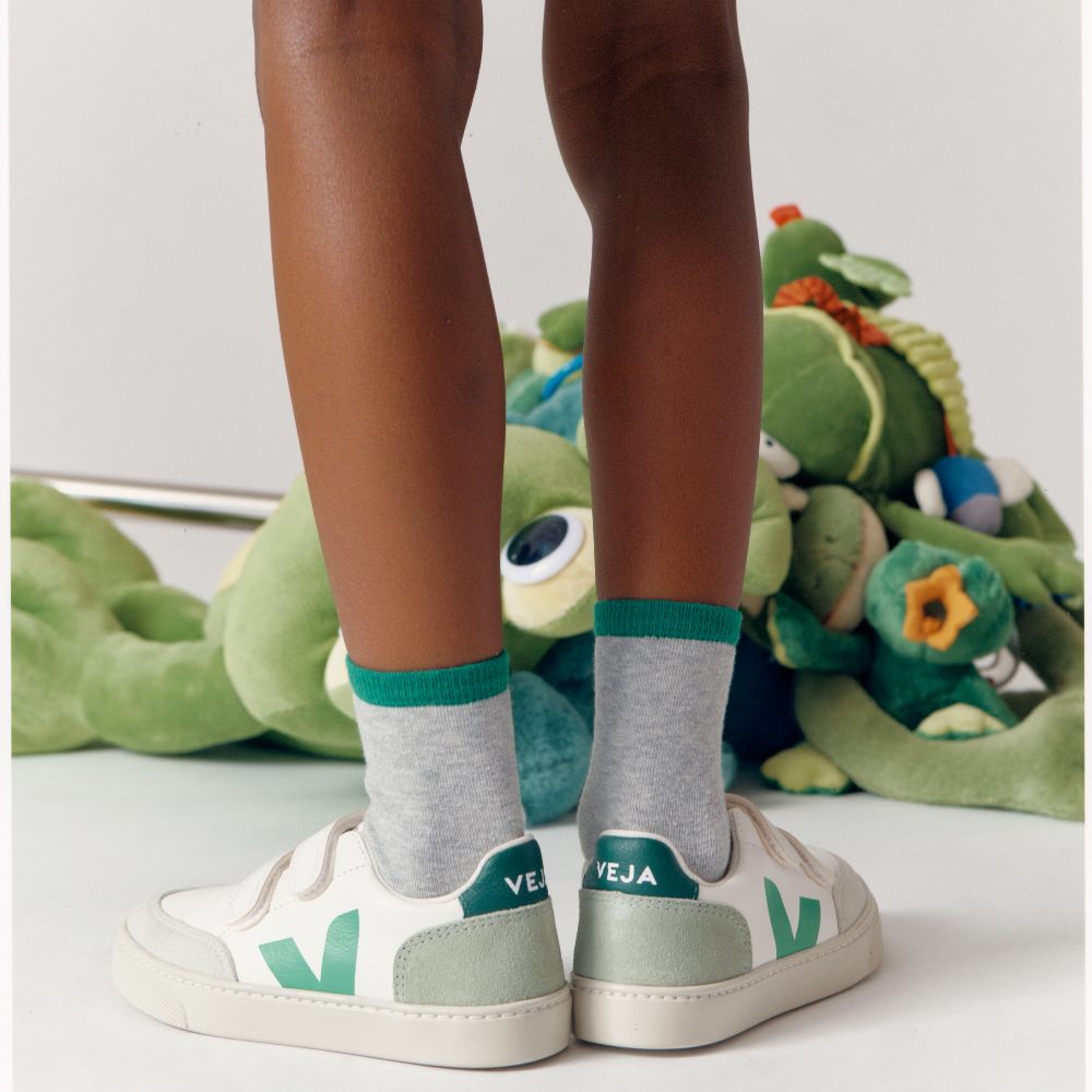 A child's legs wearing white and green Veja trainers 