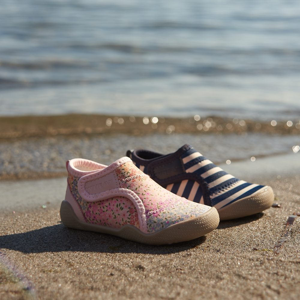 Two children's beach shoes on the sand beside the sea 