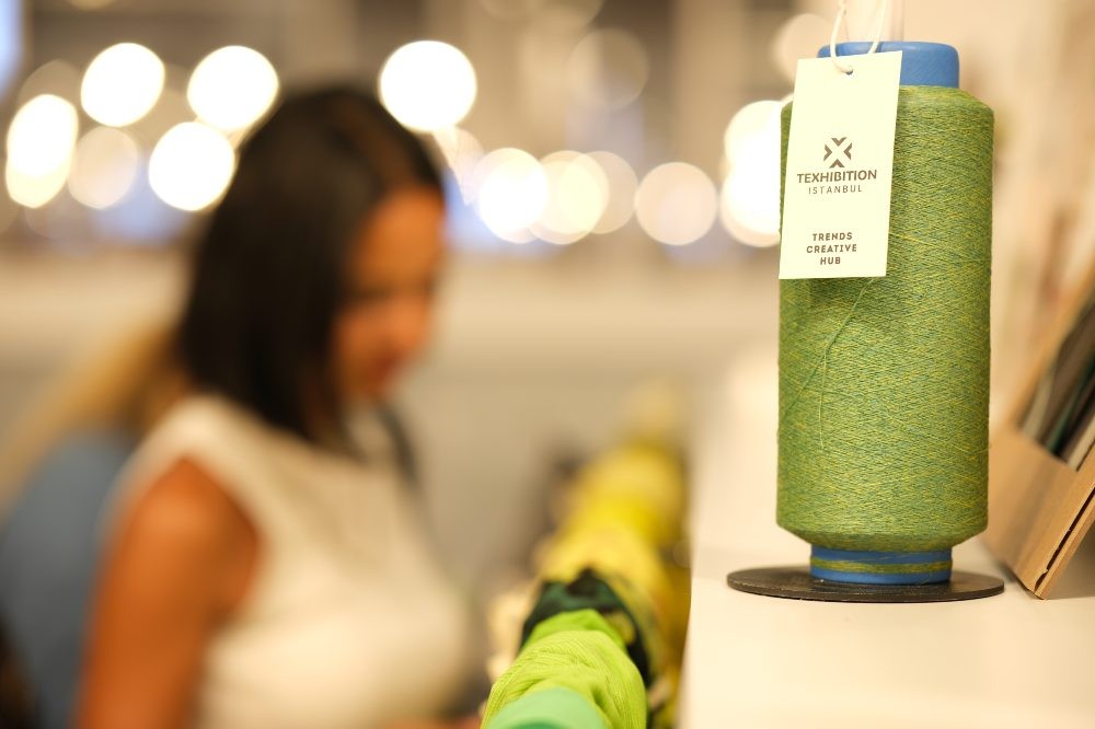 A green yarn reel on a shelf with a woman stood in the background 