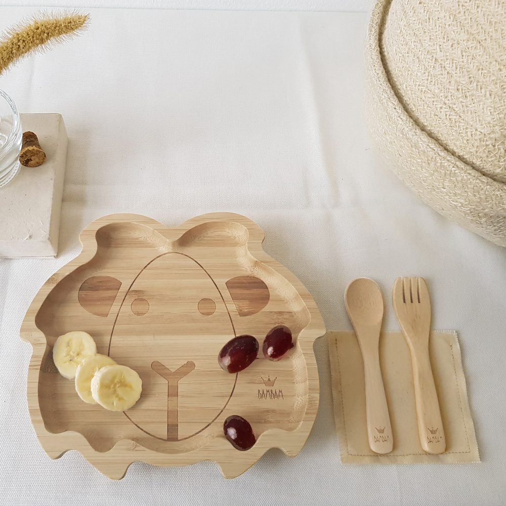 A child's wooden lion face plate and cutlery on a table 